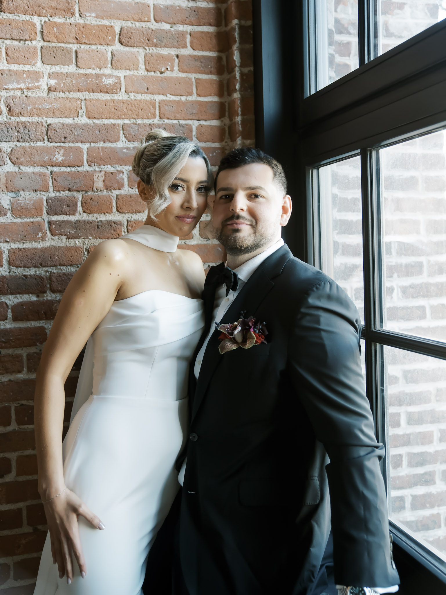 Elegant bride and groom portrait by industrial windows with exposed brick walls