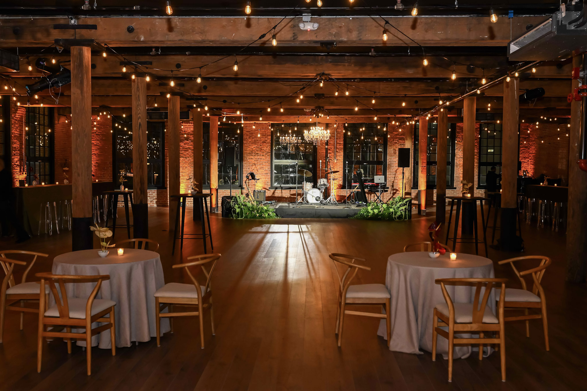 Main event space with round cocktail tables, wooden chairs, string lights, and crystal chandelier