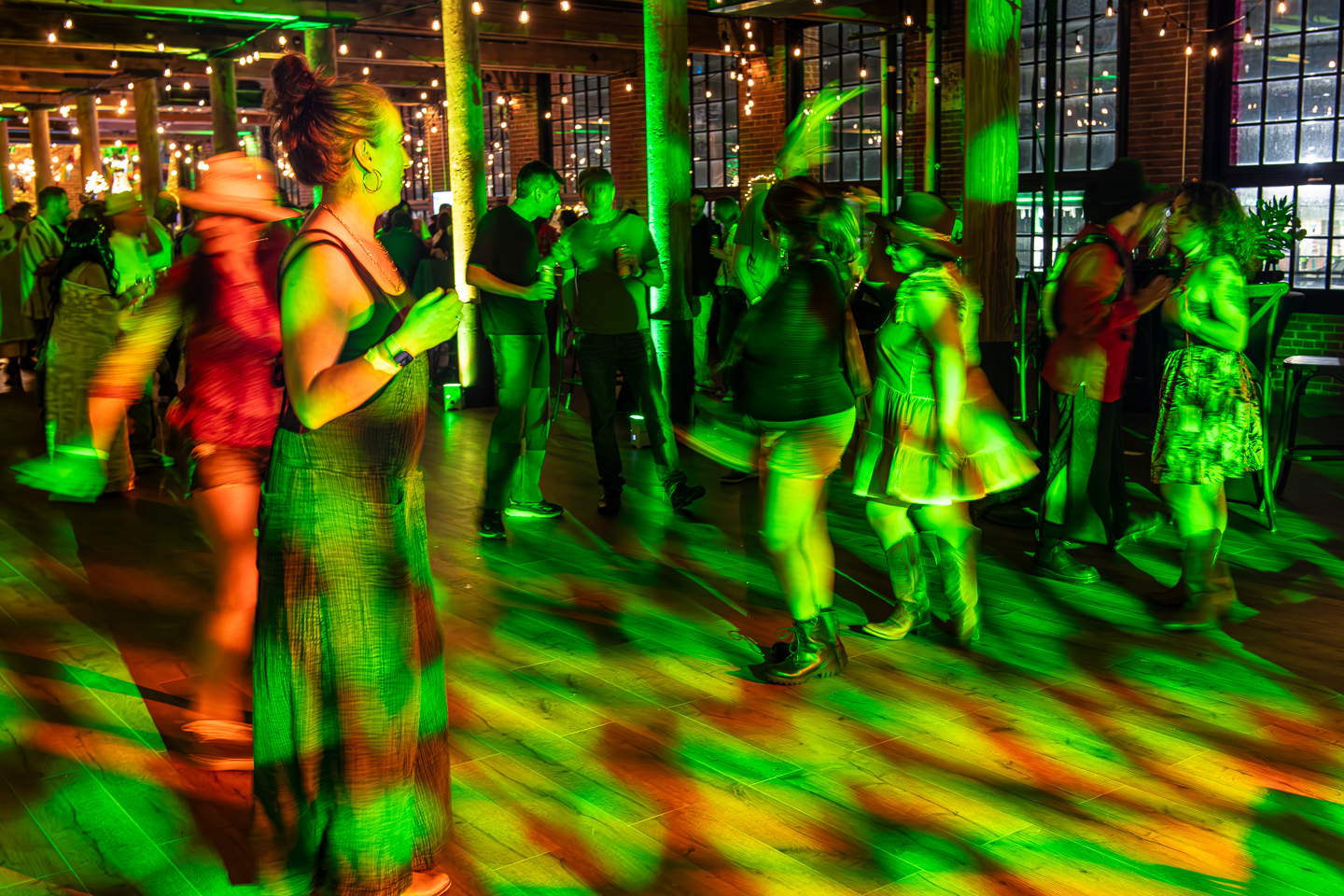 Vibrant party scene at The Mills with people dancing under colorful lighting in the industrial venue space with exposed brick walls and string lights