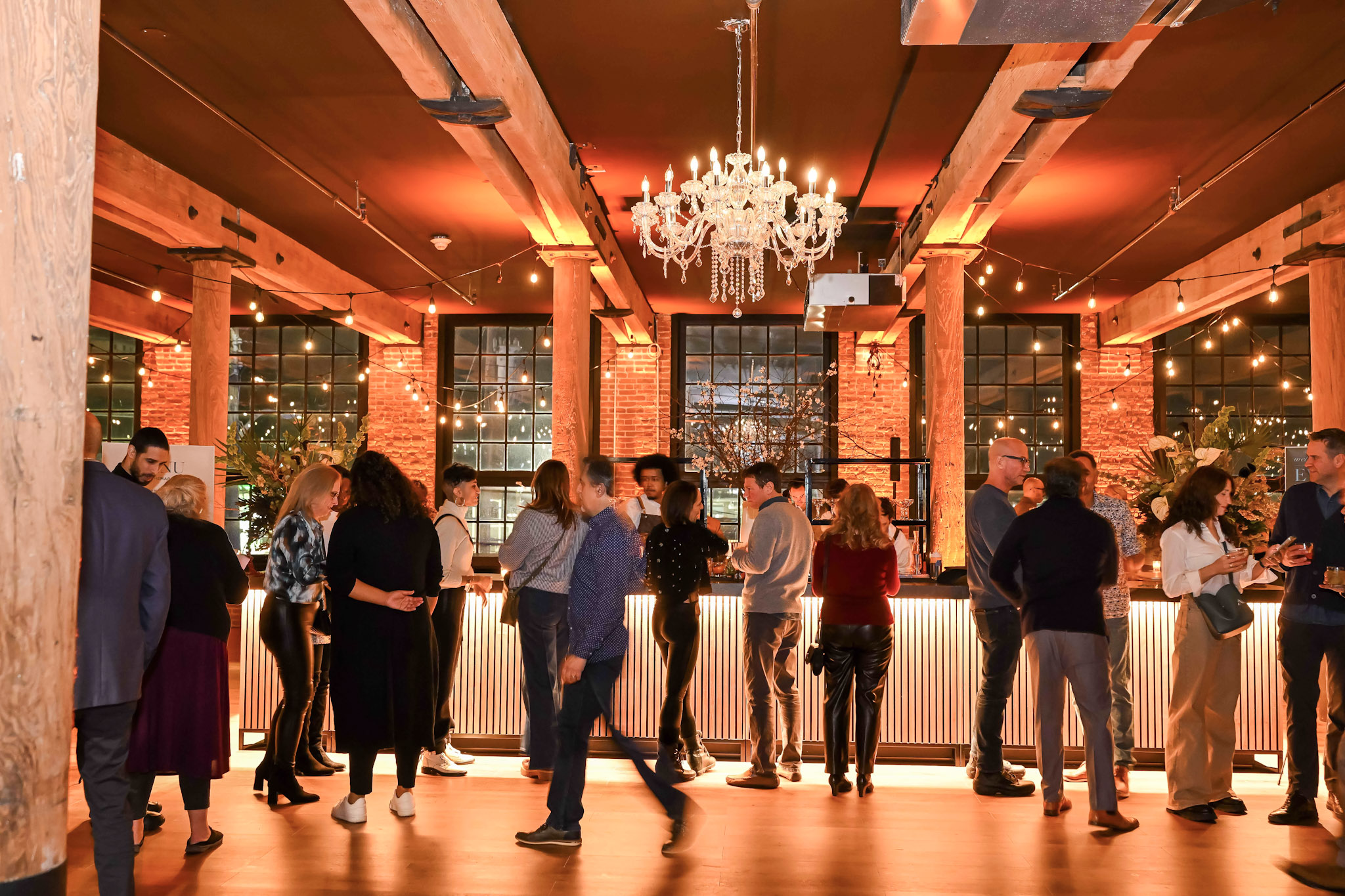 Networking cocktail event with guests mingling around illuminated bar with crystal chandelier