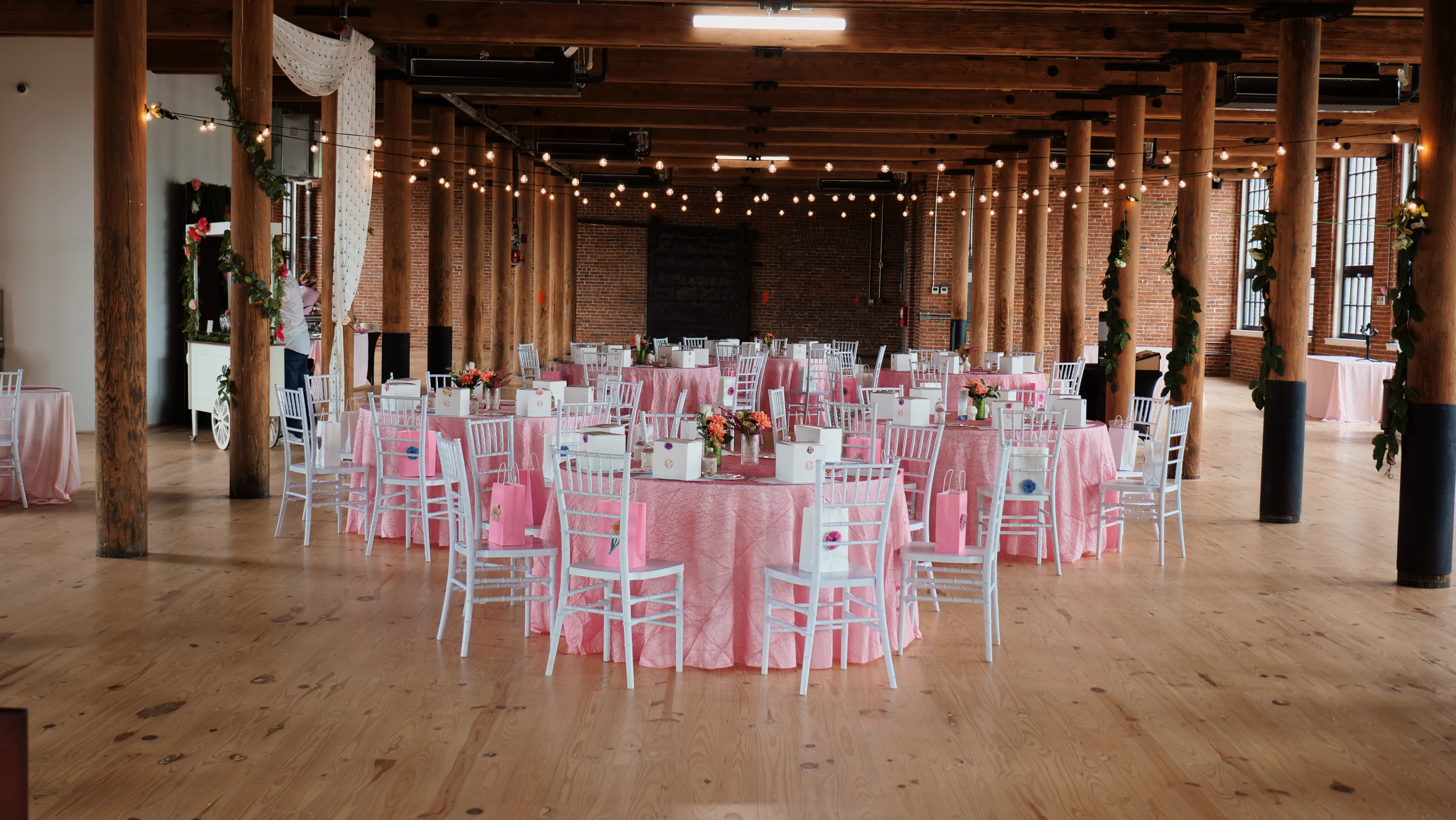 Beautiful event space at The Mills with exposed brick walls, wooden beams, string lights, and elegant pink table settings
