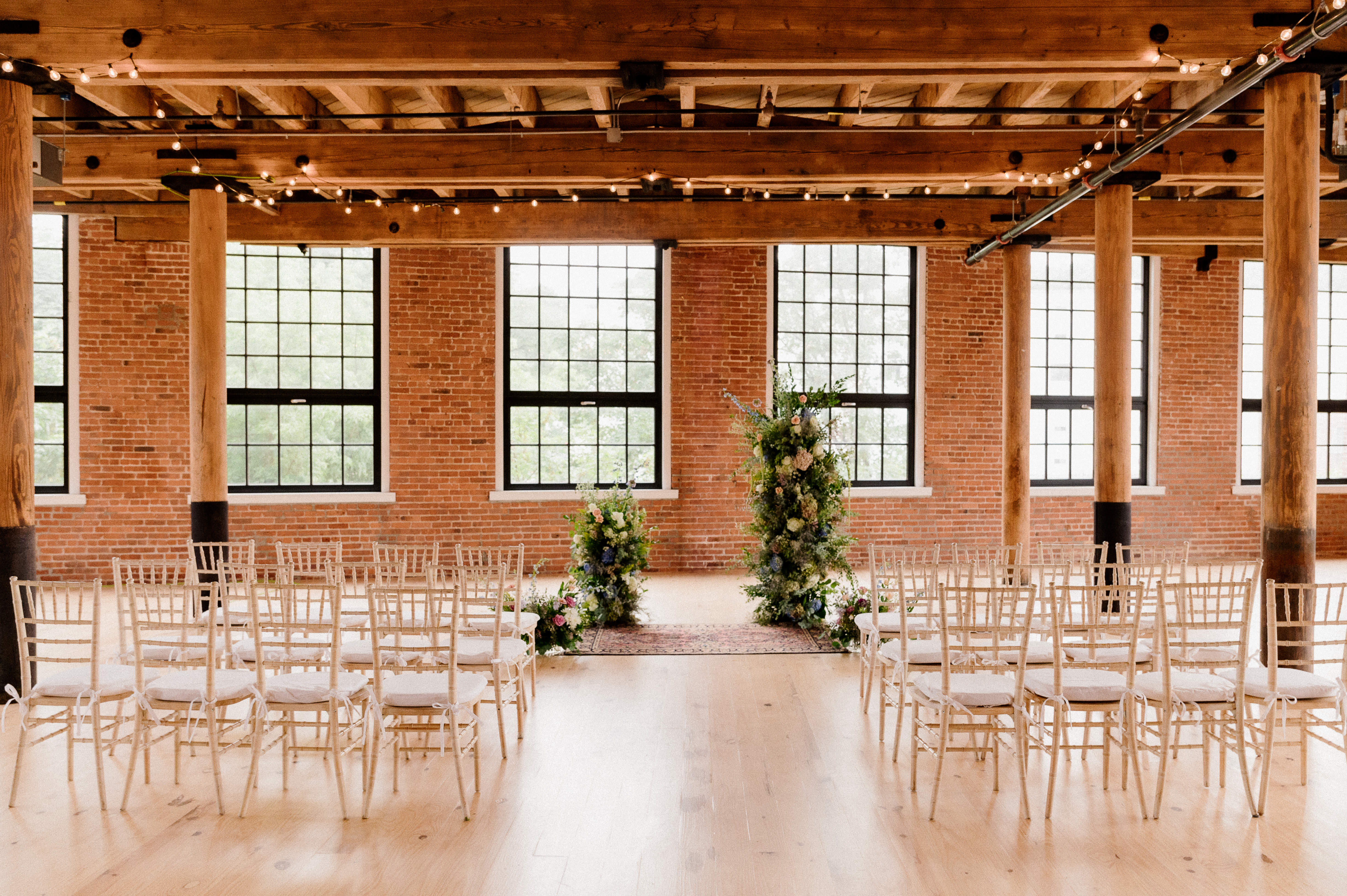 Beautiful wedding ceremony setup at The Mills with exposed brick walls, wooden beams, string lights, and elegant floral arrangements